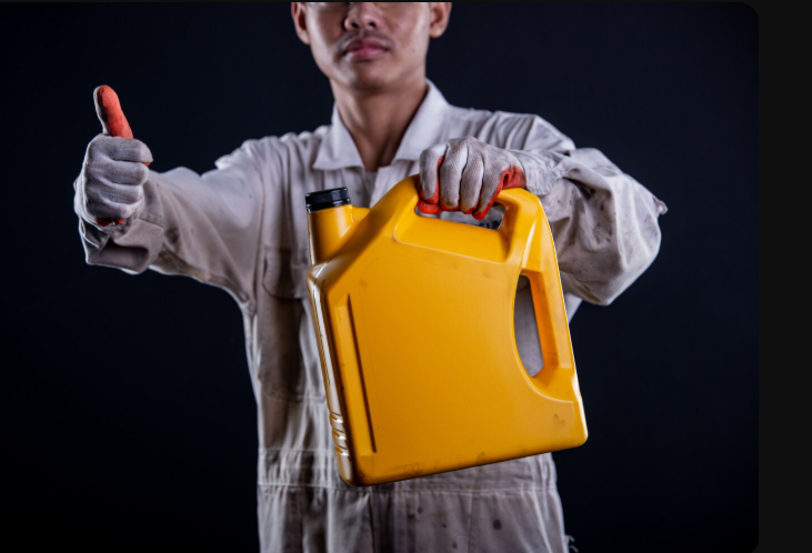 Hombre moreno con mameluco blanco y guantes de seguridad sosteniendo con la mano izquierda una galonera de líquido de frenos. Hombre moreno con mameluco blanco y guantes de seguridad sosteniendo con la mano izquierda una galonera de líquido de frenos.